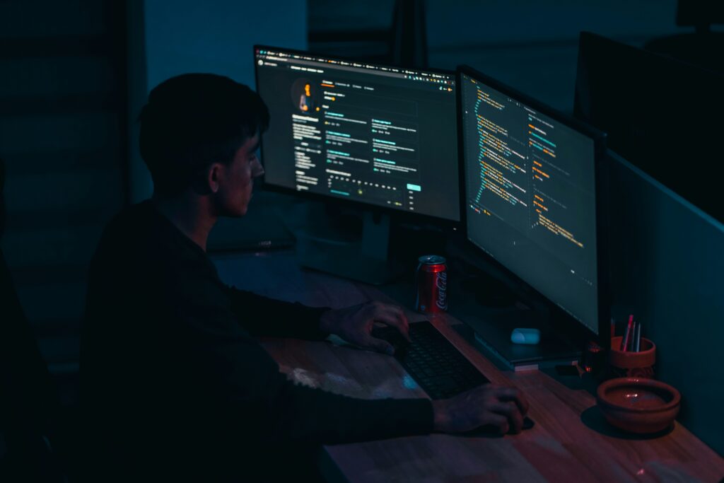 Person working at a desk with dual monitors displaying code in a dark room
